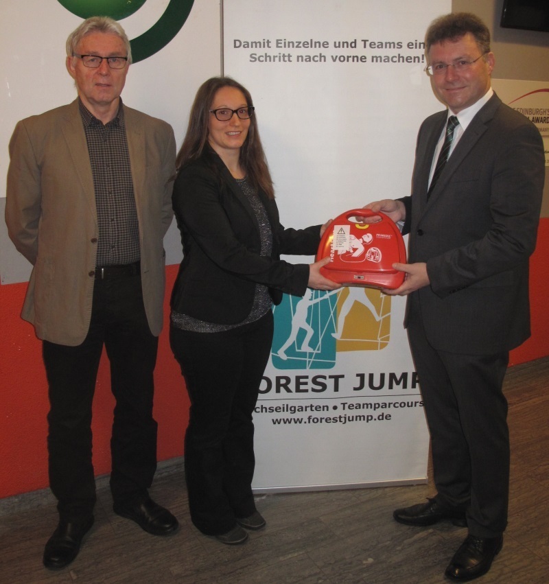 Landrat Dr. Achim Brötel, Forest Jump-Geschäftsführerin Corina Kaiser und der Direktor des Kinder- und Jugendheims St. Kilian bei der Übergabe des Automatisierten Externen Defibrillatoren. Dieser wird in Kürze in dem etablierten Hochseilgarten installiert.