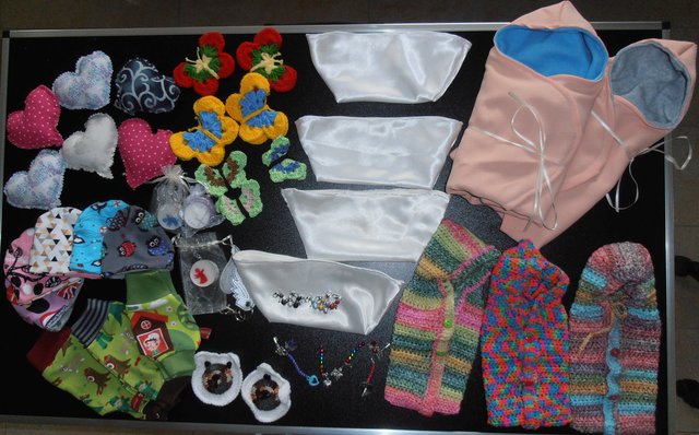 Kleine Kleidung für Frühchen, für Sternenkinder genähte und gehäkelte Einschlagdeckchen und Bestattungsschiffchen aus einem gespendeten Brautkleid sowie liebevolle Andenken für die Eltern.  Alles angefertigt von den Frauen der Nähgruppe Leander. 
