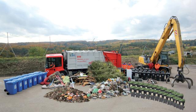 Beispielfoto (Montage) der Abfallmengen, die der neuen Standard-Abfallgebühr von 203,95 € entsprechen
(von links): Altpapier, Sperrmüll, Bioabfall, Altholz, Grüngut, Restmüll (vorne), Elektronschrott, Altmetall sowie die dazugehörigen Abfalltonnen entsprechend den jährlichen Leerungen (13 bzw. 26). Foto: KWiN