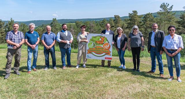 Matthias Dick und Marion Münz (beide Sparkasse, rechts und links neben der Plakette) übergaben im Beisein von Landrat Jens Marco Scherf (zweiter von rechts), Kitzrettungsinitiatorin Doris Völker-Wamser und weiteren Aktiven große Plaketten an Leidersbacher Bürgermeister Michael Schüßler (vierter von links).