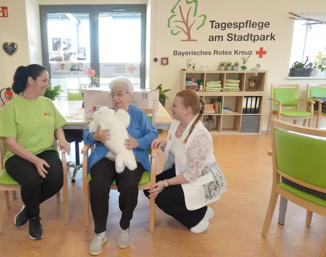 Eine Seniorin freut sich mit zwei BRK-Pflege-Mitarbeiterinnen über Robbie, die neue Anschaffung.
