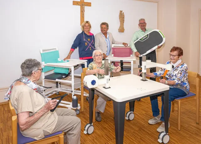 Drei Bewohnerinnen des Seniorenheims Maria Regina trainieren am Plaudertisch, beobachtet von (hinten von links) Miriam Krebes (Pflegedienstleitung), Einrichtungspate Elmar Miksche und Einrichtungsleiter Matthias Schiller, der eine Vibrationsplatte zeigt, mit der die Muskulatur gestärkt werden kann. | Foto: Winfried Zang