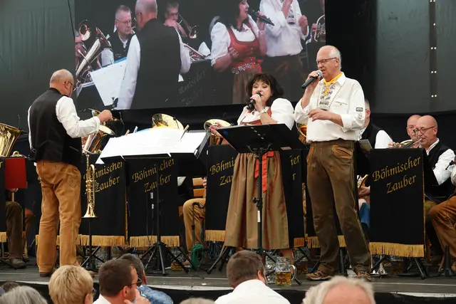 Am ersten Messe-Sonntag spielten sie im Festzelt um die Mittagszeit drei Stunden lang: die Musikerinnen und Musiker vom „Böhmischen Zauber“, fast zwei Dutzend an der Zahl, unter der bewährten Leitung von Herbert Herrmann und dem Gesangsduo und Moderatoren-Team Rita Barth und Hans Heil. 