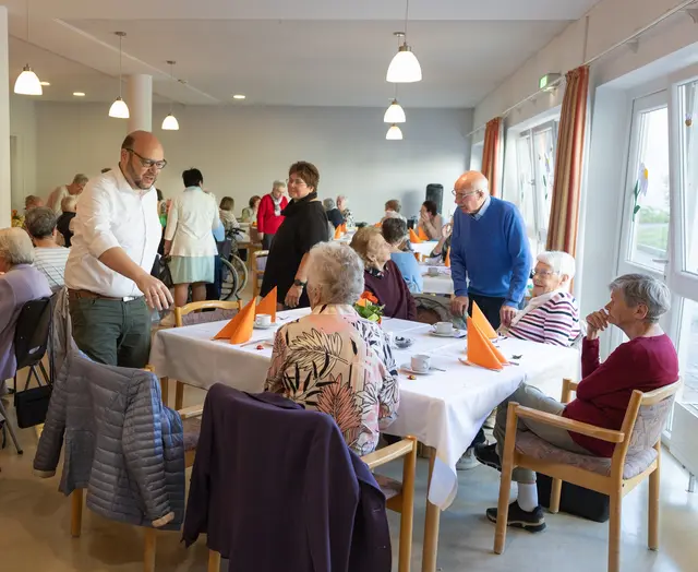 Das Bild zeigt den begrüßenden Bürgermeister Dörr und eine sitzende Menschengruppe 
