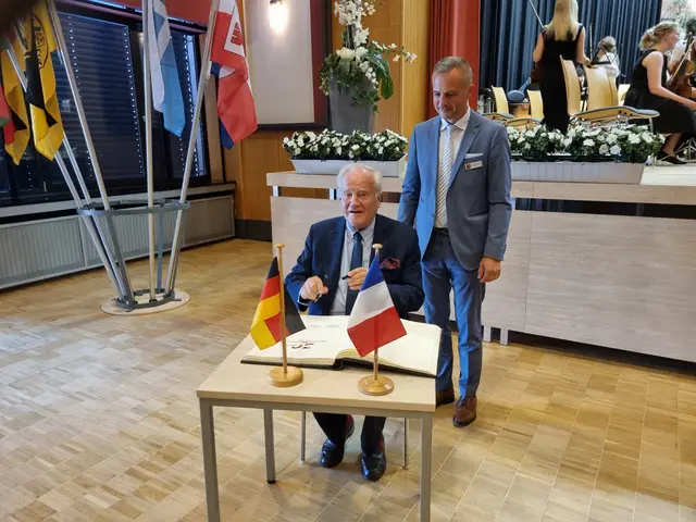 Sénateur Christian Cambon (sitzend) trägt sich in das Goldene Buch der Stadt Erlenbach a.Main ein. Rechts daneben Erster Bürgermeister Christoph Becker. | Foto: Stadt Erlenbach