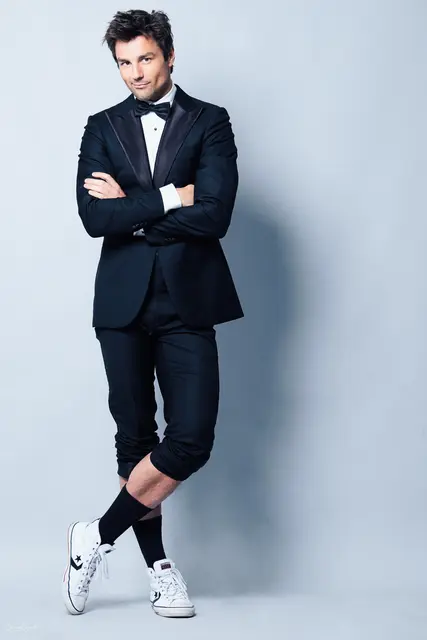 Das Bild zeigt den Künstler und Comedian Lars Redlich vor einem blauen Hintergrund in lockerer Pose stehend